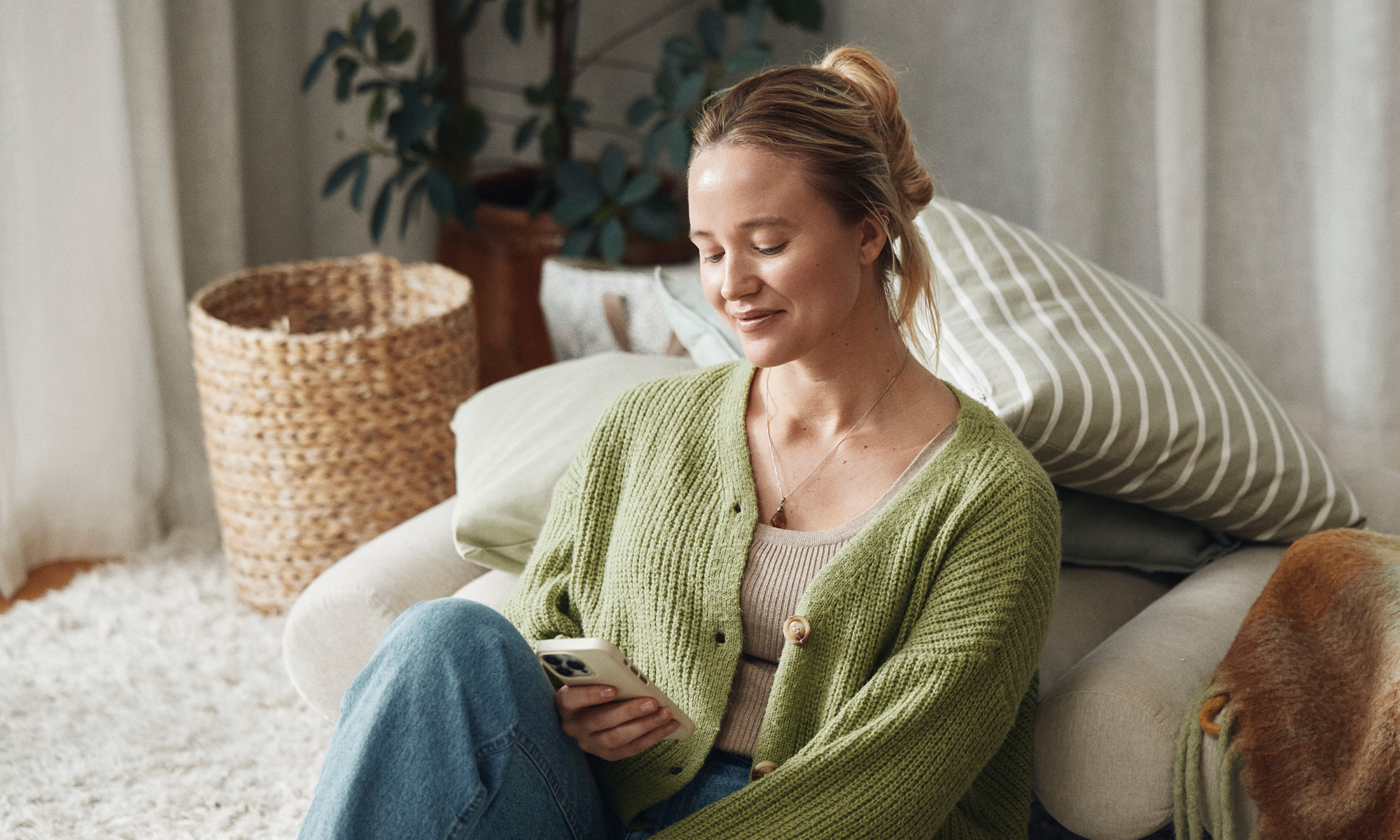 En ung tjej sitter i sin soffa och tittar i mobilen
