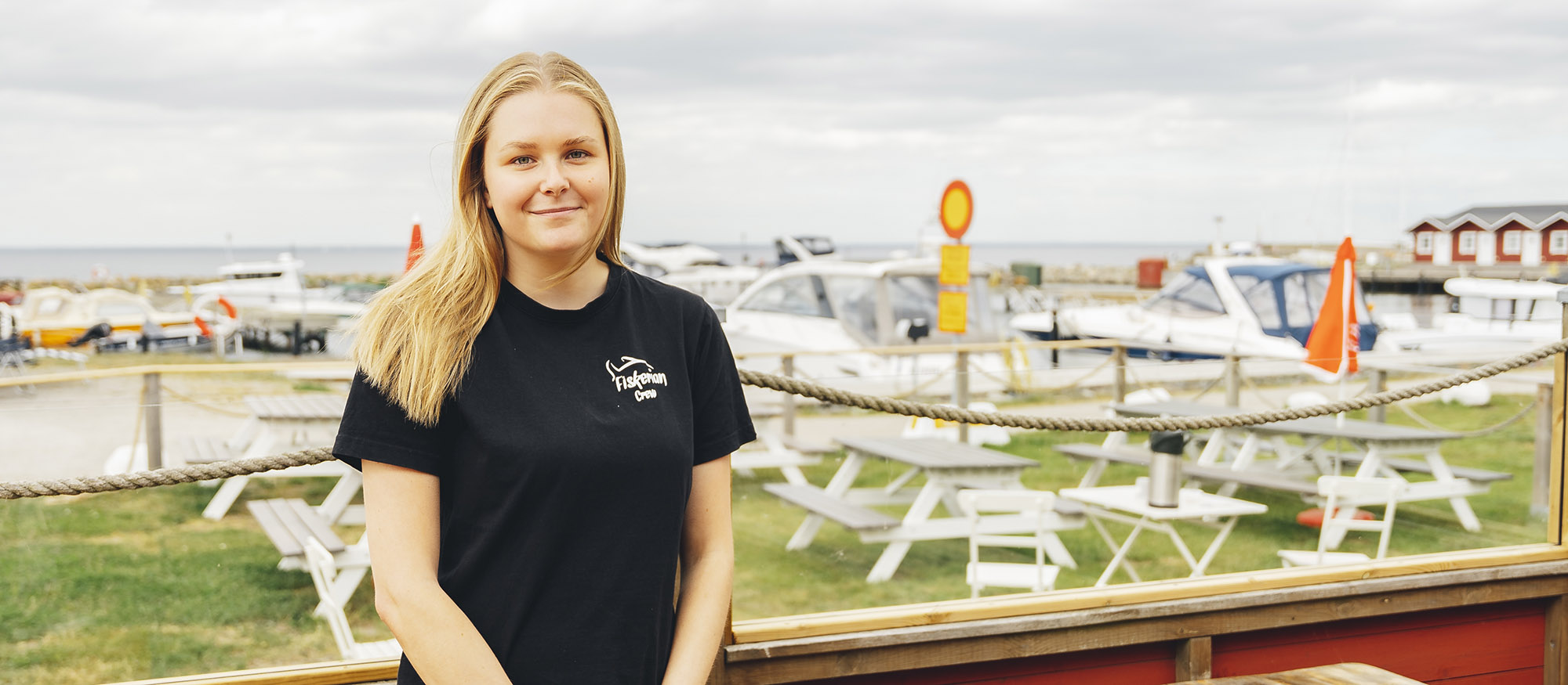 Jasmine står på uteserveringen med småbåtshamnen i bakgrunden