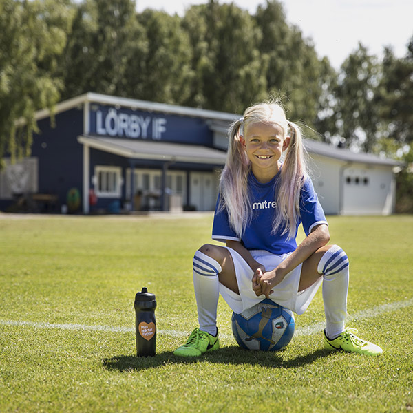 Flicka sitter på en fotboll på Lörby Park