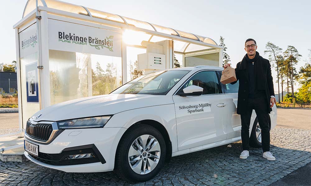 Oscar står framför bankens biogasbil vid en tankstation.