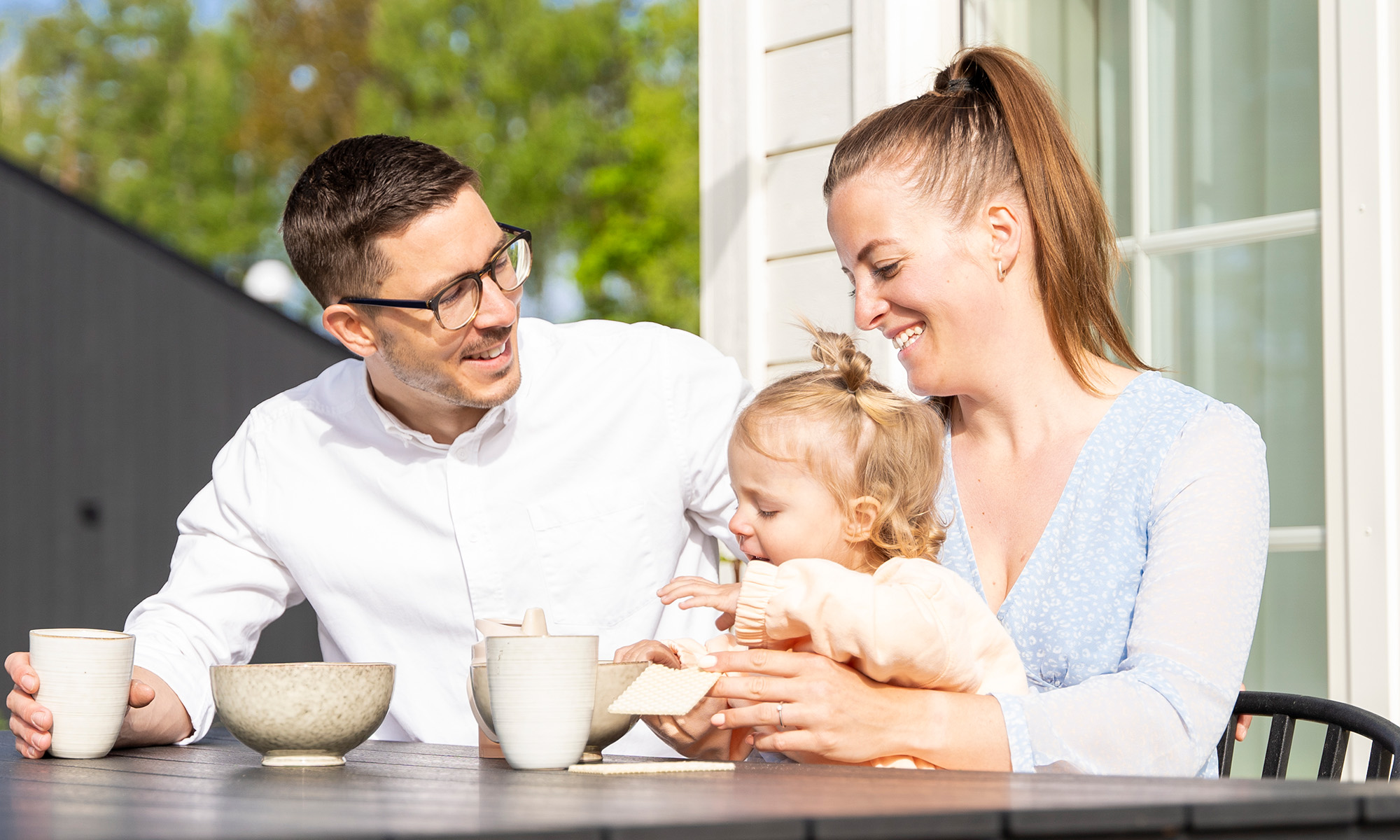 Mamma, pappa och dotter sitter och fikar i solen på sin uteplats
